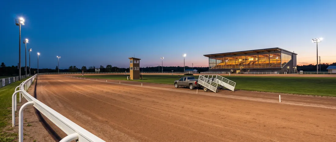 Empty harness racing oval and lit grandstand at blue hour